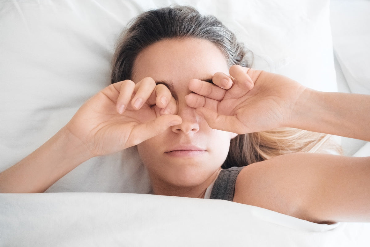 Frau liegt im Bett und reibt sich die Augen