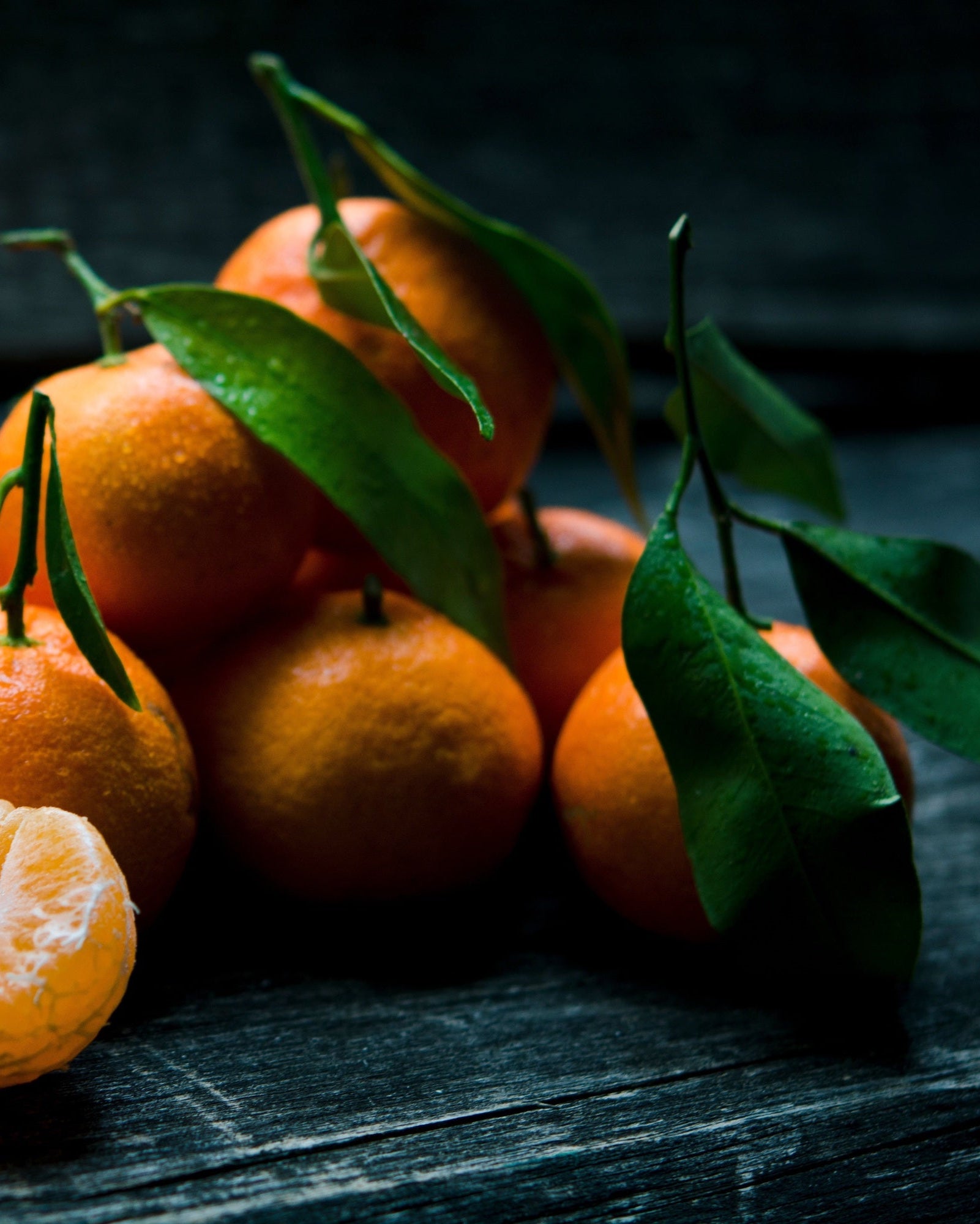 Reife Orangen mit Stil und Blättern liegen auf einem dunklen Holztisch