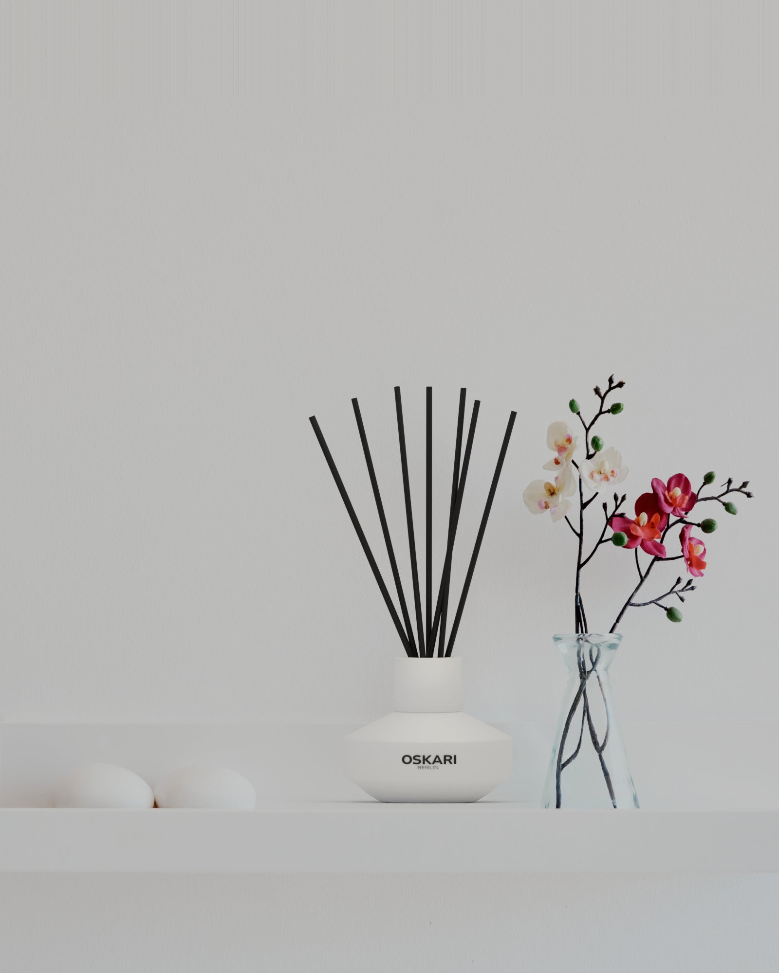 Oskari weisser Opalglasflakon mit schwarzen Duftstäbchen auf minimalistischem weissen Ragalboden mit Orchideen und weissen Designsteinen