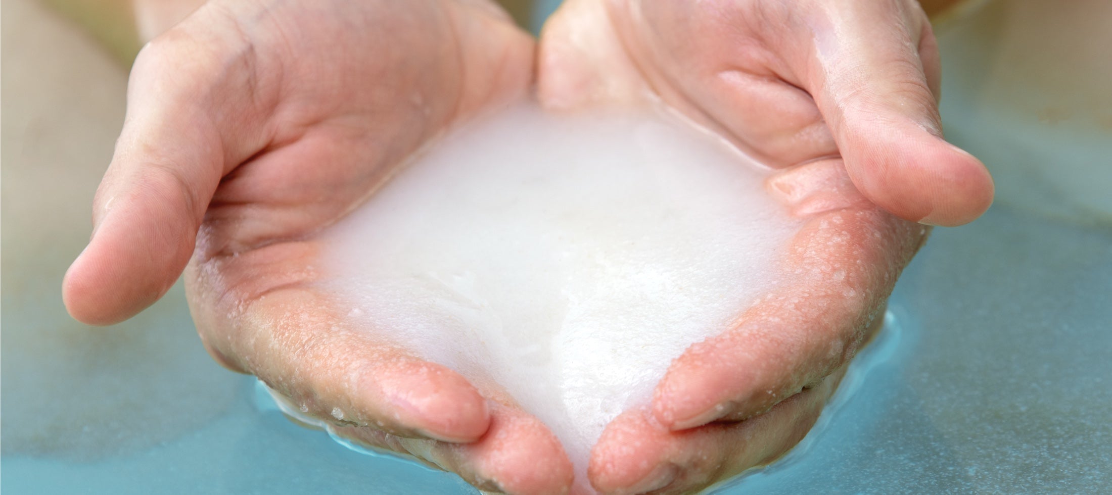 Helle Salz-Wasserlösung in gespreizten Händen über blauem Wasser