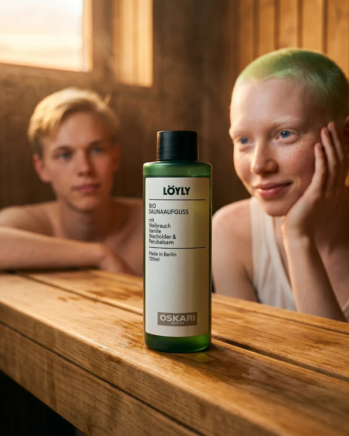 Der Bio Saunaaufguss Löyly von Oskari in einer Sauna mit einer jungen Frau mit grünen Haaren und einem Jungen Mann im Hintergrund