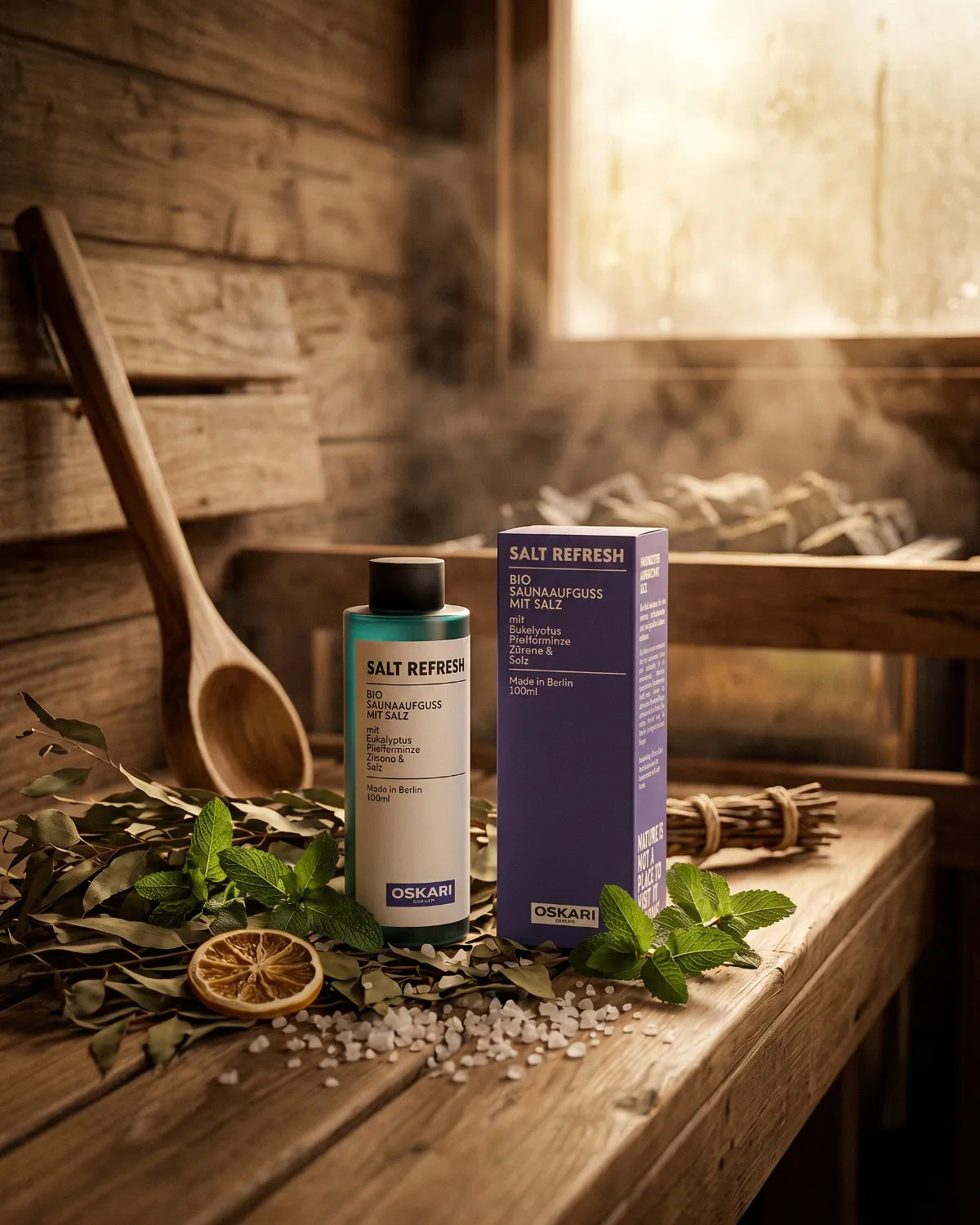 Oskari Bio Salzaufguss Salt Refresh mit Salz und Pflanzen in einer Holzsauna mit Dampf über dem Saunaofen