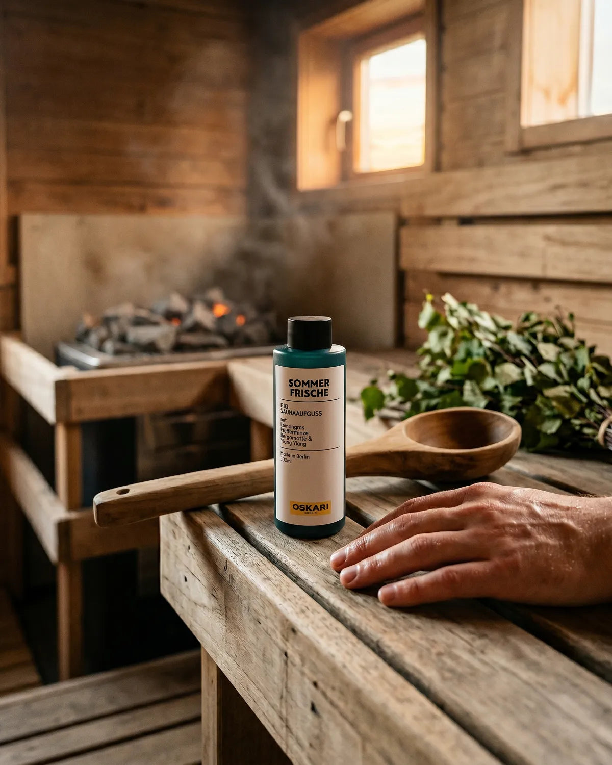 Eine Flasche Sommerfrische Bio Saunaaufguss von Oskari in der Sauna neben einer Hand und einer Holzkelle