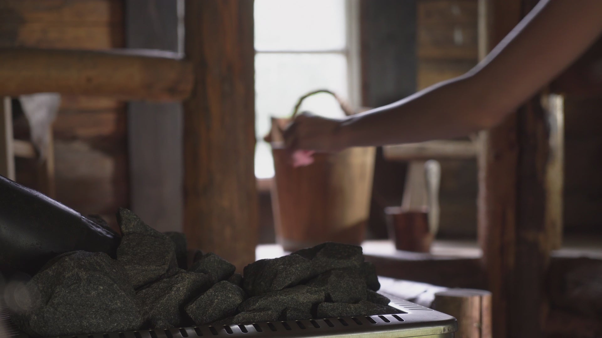 Video laden: Eine Frau mit langen Haaren bereitet einen Saunaaufguss vor indem sie Wasser mit einer Holzkelle über den heissen Saunasteinen verteilt - Dampf steigt auf