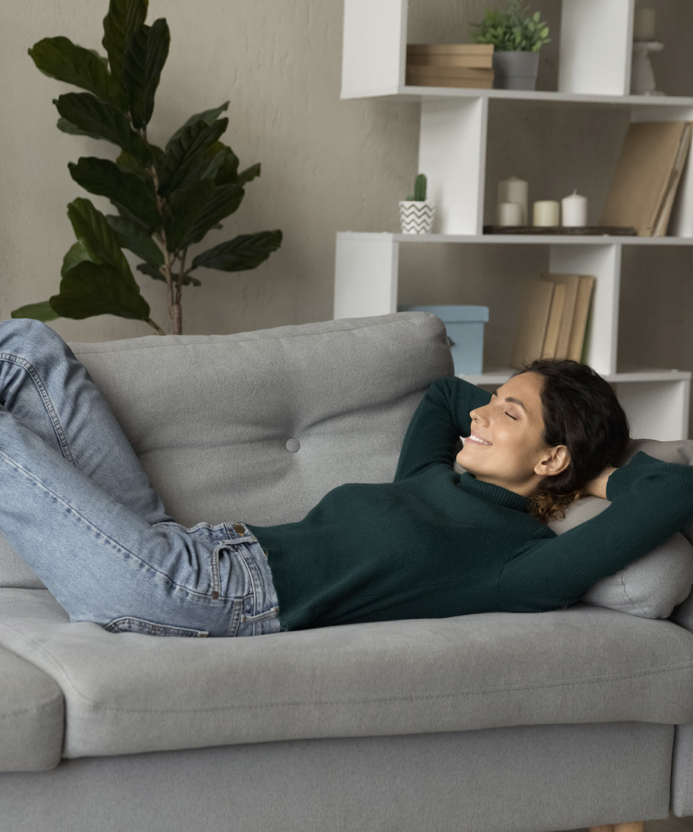 Eine dunkelhaarige junge Frau entspannt auf ihrem grauen und gemütlichen Sofa