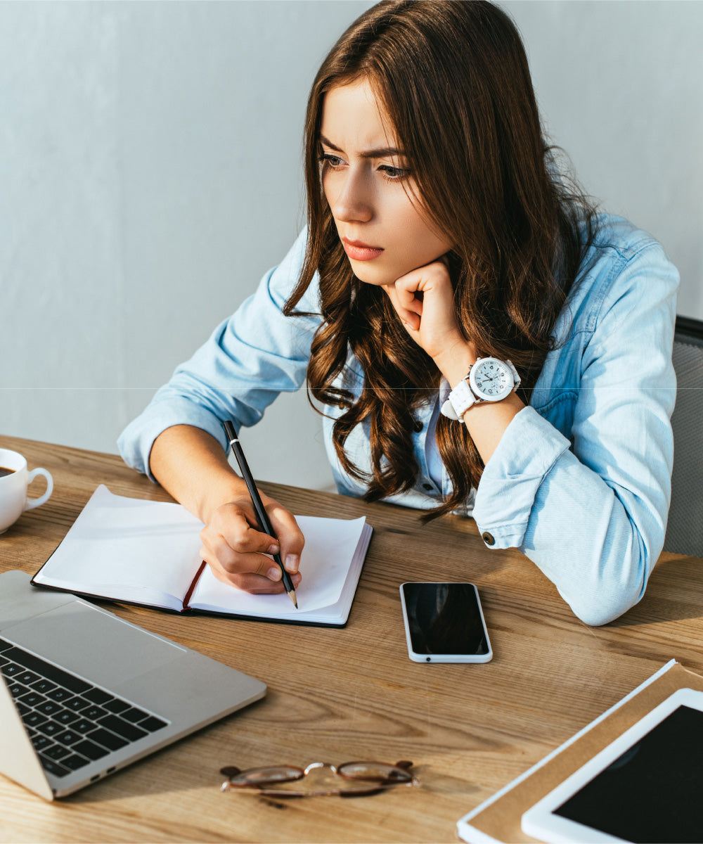 Junge dunkelhaarige Frau schaut konzentriert auf ihren Laptop der auf einem hölzernen Schreibtisch steht