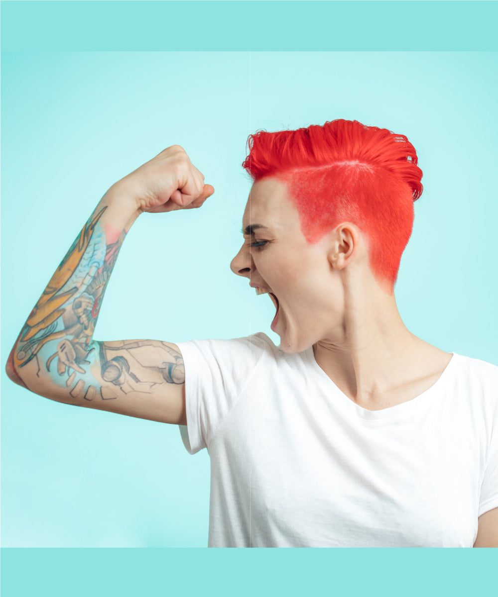 Starke junge Frau mit kurzen roten Haaren und tätowierten Armen ballt ihre Faust