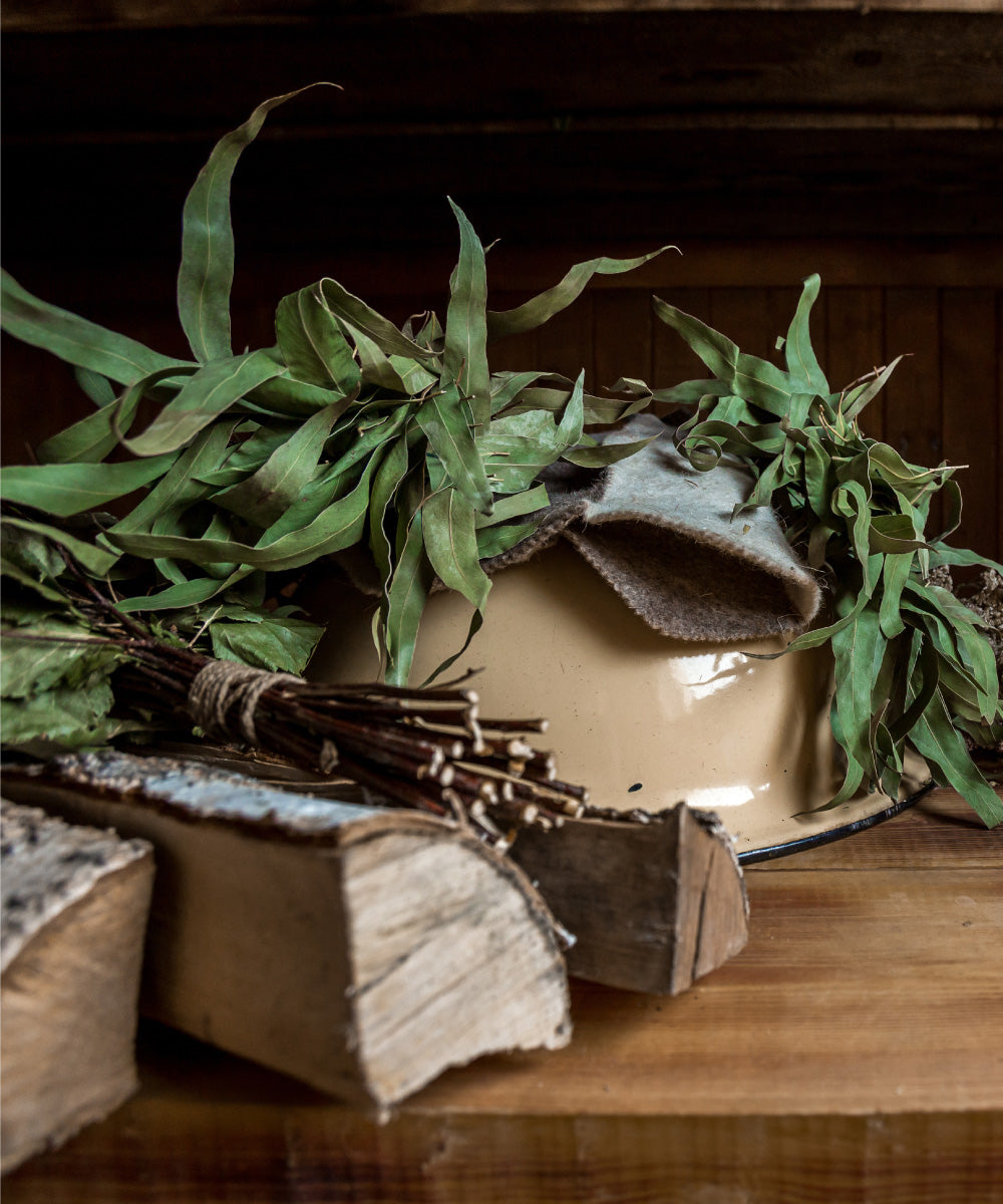 Verschiedner Kräuter und Holzscheite liegen auf einem schweren hölzernen Tisch mit einer Emailleschüssel darauf