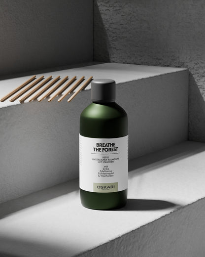 Auf grauer Betonstufe stehend die Nachfüllflasche für den Oskari Raumduft Breathe the Forest und die zugehörigen acht Duftstäbchen aus nachhaltigem Papier.