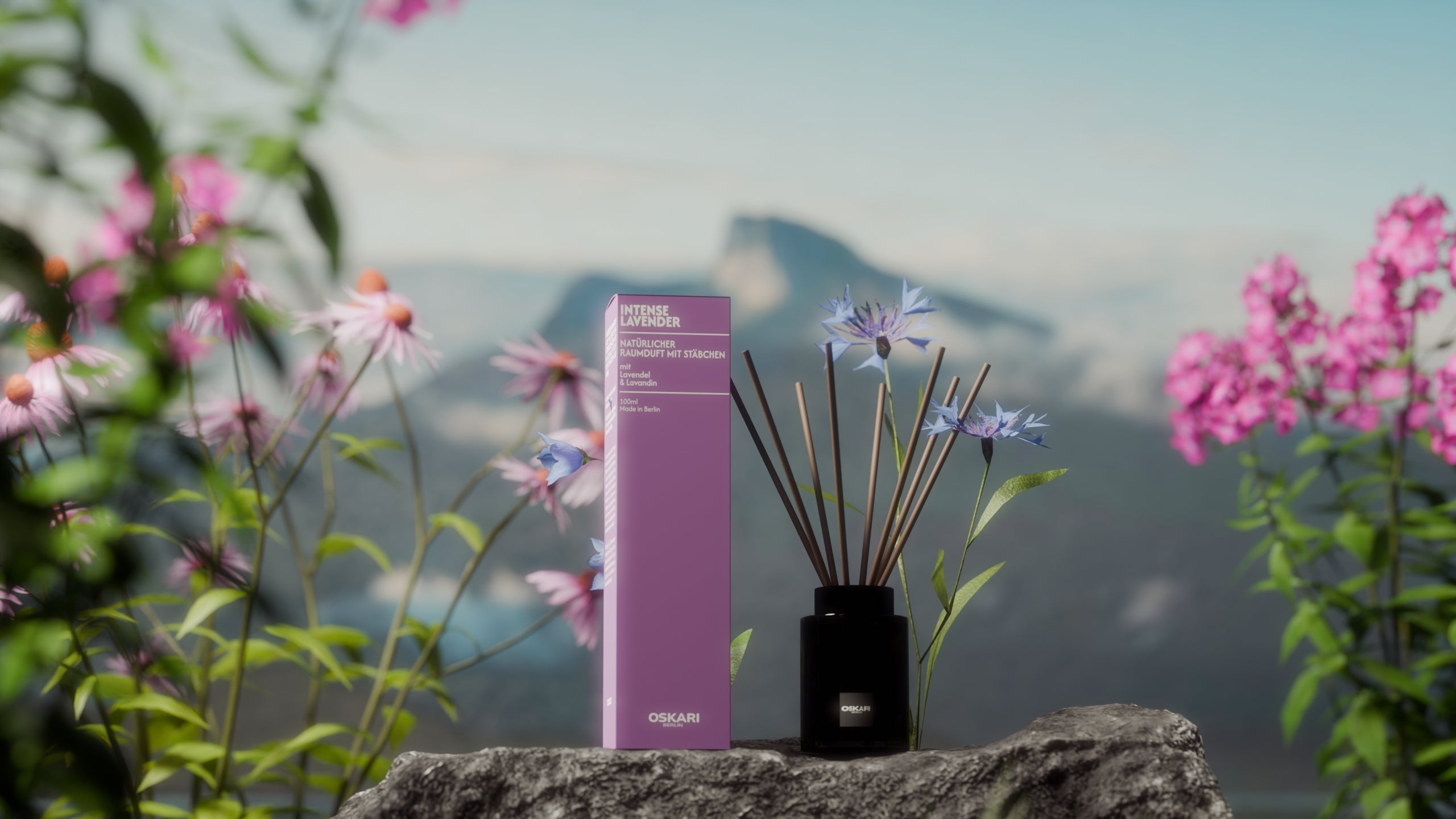 Der Oskari Raumduft mit Stäbchen Intense Lavender auf einem Stein mit Bergpanorama und bunten Blüten