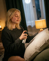 Eine junge blonde Frau in einem schwarzen Wollpulli sprüht das Bio Kissenspray Berlin Nights von Oskari auf ein Kopfkissen in ihrem Schlafzimmer