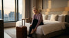 Eine Frau zieht sich ihre Schuhe auf einem Hotelbett neben ihrem Koffer aus um schlafen zu gehen