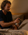 Ein Mann sitzt im Bett und benützt das Oskari Bio Kissenspray Dreametime Blend