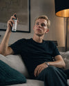 Ein junger Mann sitzt relaxt auf einem Sofa und versprüht das Bio Raumspray Cill Zone von Oskari
