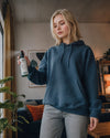 Junge Frau im blauen Hoodie versprüht das Bio Raumspray Shinrin Yoku von Oskari in ihrer Wohnung