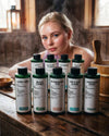 Junge Frau sitzt in der Sauna vor den Flaschen der neun Bio Saunaaufgüsse des  Bestseller Bundles von Oskari