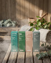 Das Oskari Bio Saunaaufguss Bundle Classic Collection in den bunten Schachteln mit den Aufgüssen Alpen Zirbe, Black Forest, Entspannung Pur und Kräuter Kick in eiuner dampfgefüllten Sauna