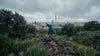 Eine Frau im Mantel und inmitten von Natur steht vor der Berliner Skyline mit Dom und Fernsehturm.
