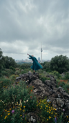 Eine Frau im Mantel und inmitten von Natur steht vor der Berliner Skyline mit Dom und Fernsehturm.