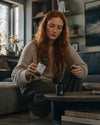 Der natürliche Raumduft mit Stäbchen von Oskari Positive Thinking in  der Hand einer rothaarigen jungen Frau auf dem Dielenboden ihres Wohnzimmers